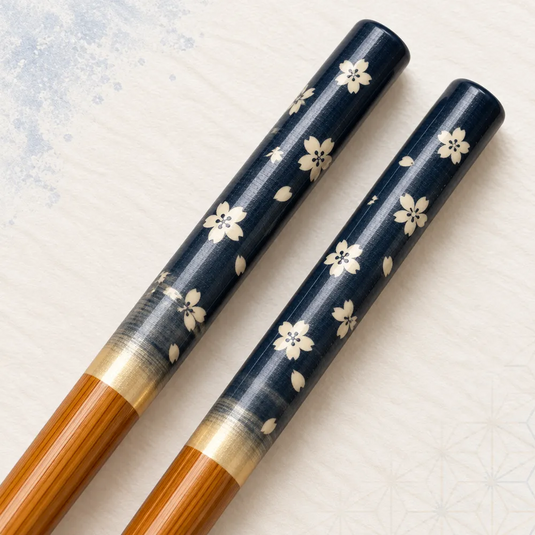 Très gros plan des fleurs de cerisier claires et des pétales imprimés sur les manches bleu profond des baguettes japonaises Sakura Ao.
