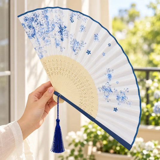 Éventail japonais Hana à fleurs bleues tenu en main et incliné, avec son pompon bleu foncé suspendu.