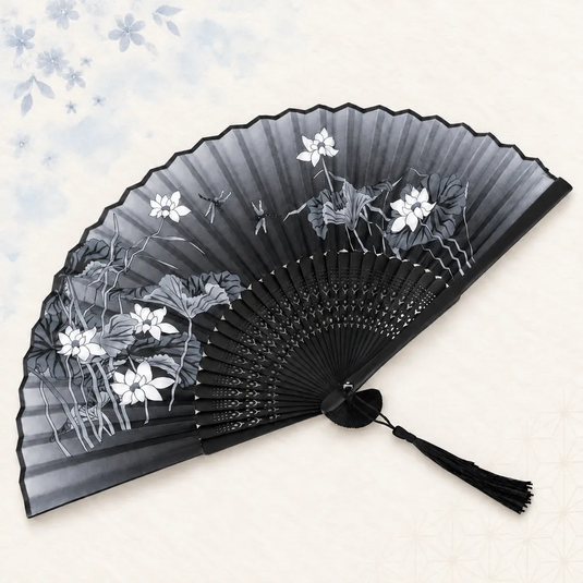 Éventail japonais noir et gris ouvert, décoré de fleurs blanches, de feuillages et de libellules, avec un pompon noir.