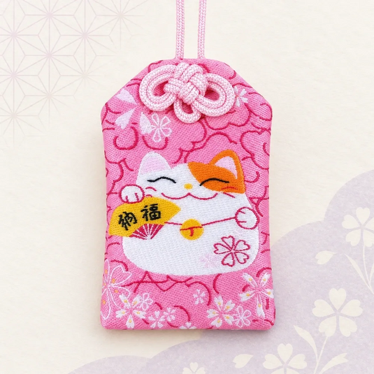 Omamori japonais rose de bonheur et de chance, brodé d’un Maneki-neko blanc et orange, vue de face.