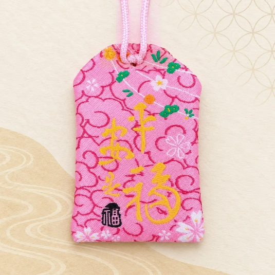 Verso de l’omamori japonais rose Maneki-neko, avec calligraphies jaunes et double cordon rose.