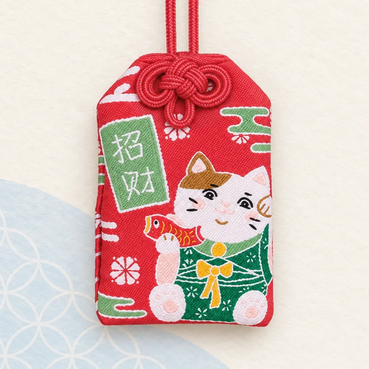 Omamori japonais rouge avec un chat neko en kimono vert tenant un poisson, et une inscription blanche.