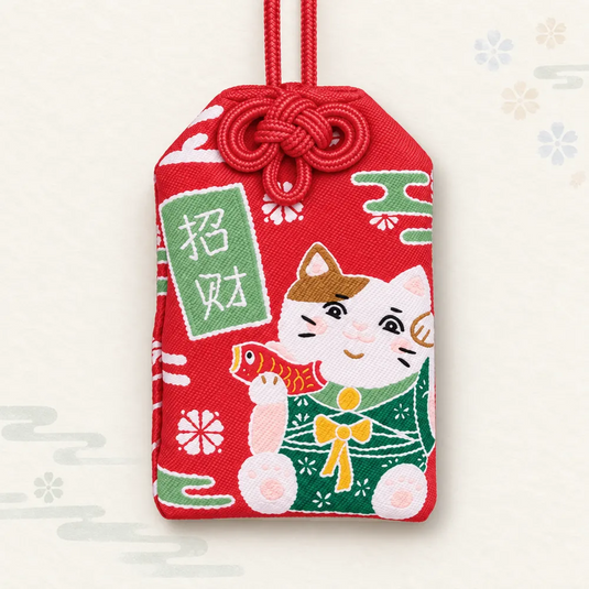 Omamori japonais rouge avec un chat neko en kimono vert tenant un poisson, et une inscription blanche.