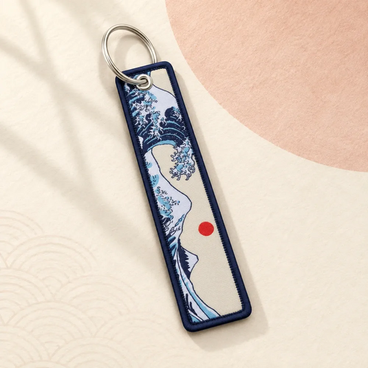 Porte-clés japonais en tissu à motif de vague Hokusai, avec bordure bleu marine et anneau argenté.