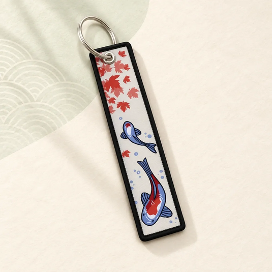Porte-clés japonais en tissu avec deux carpes koï bleues et rouges, des feuilles d’érable et une bordure noire.