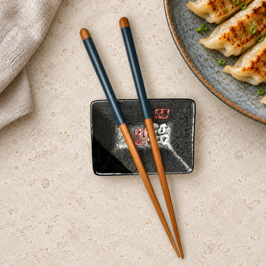 Baguettes japonaises Ao aux manches bleus, posées côte à côte sur un repose-baguettes près d’une assiette de gyoza.