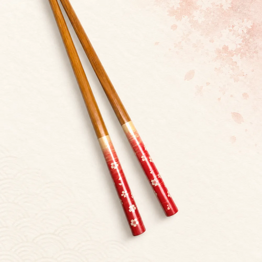Vue rapprochée des fleurs claires sur les manches rouges des baguettes japonaises Sakura Aka, avec leur transition dorée vers le bambou.