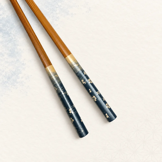 Vue rapprochée des fleurs claires sur les manches bleu profond des baguettes japonaises Sakura Ao, avec leur transition dorée vers le bambou.