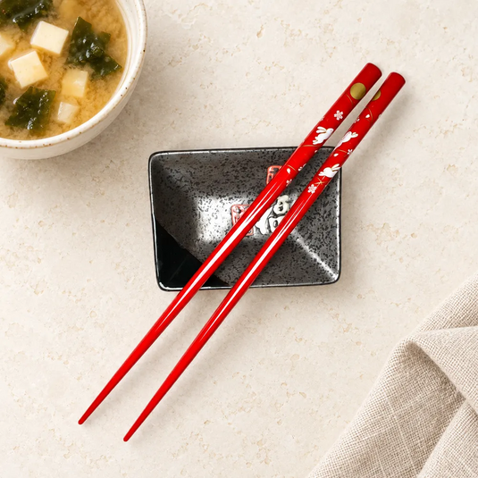 Baguettes japonaises Usagi rouges sur une coupelle noire, près d’un bol de soupe miso.