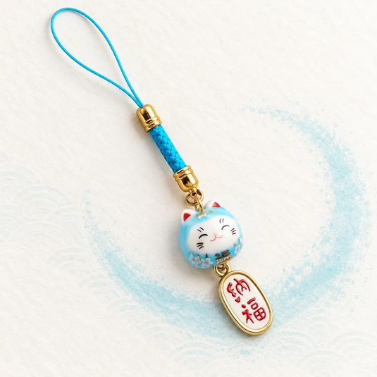 Bijou de téléphone Maneki Neko Aoi avec chat bleu clair, cordon turquoise et pendentif ovale ivoire bordé d’or.