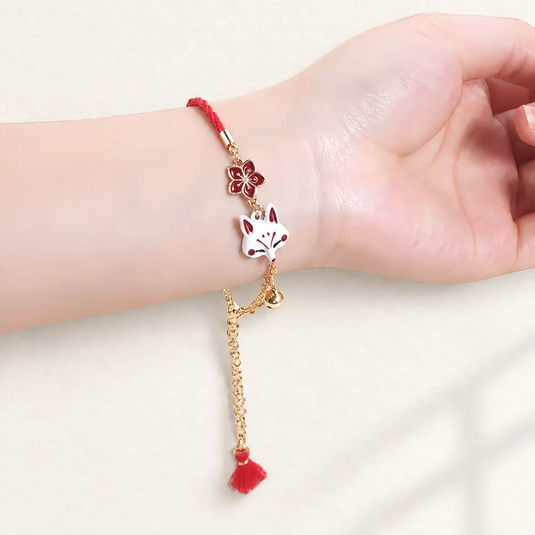 Bracelet japonais Kitsune rouge porté au poignet, avec masque de renard blanc et breloques dorées.