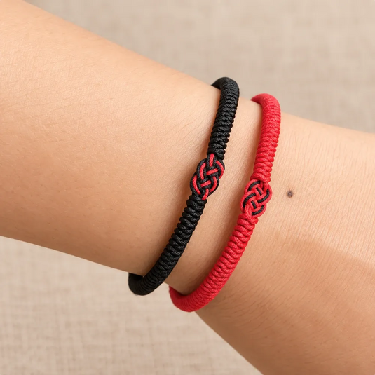 Bracelets bouddhistes rouge et noir portés côte à côte au poignet, avec leurs nœuds bicolores.