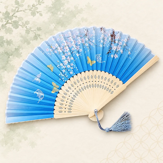 Éventail japonais Chōchō bleu ouvert, avec fleurs blanches, papillons, monture en bambou clair et pompon bleu-gris.