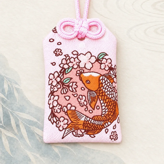 Omamori japonais rose de bonne fortune, brodé d’une carpe koï orange et de fleurs de cerisier, vue de face.