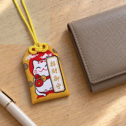Omamori Maneki-neko doré posé sur un bureau à côté d’un portefeuille.