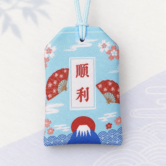 Verso de l’omamori japonais bleu aqua pâle, avec inscription rouge, éventails et mont Fuji.