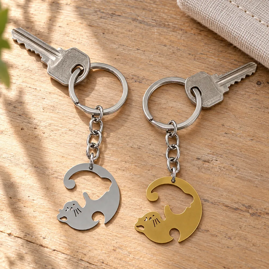 Deux porte-clés chats Neko Yin Yang, argenté et doré, chacun attaché à une clé sur une table en bois.